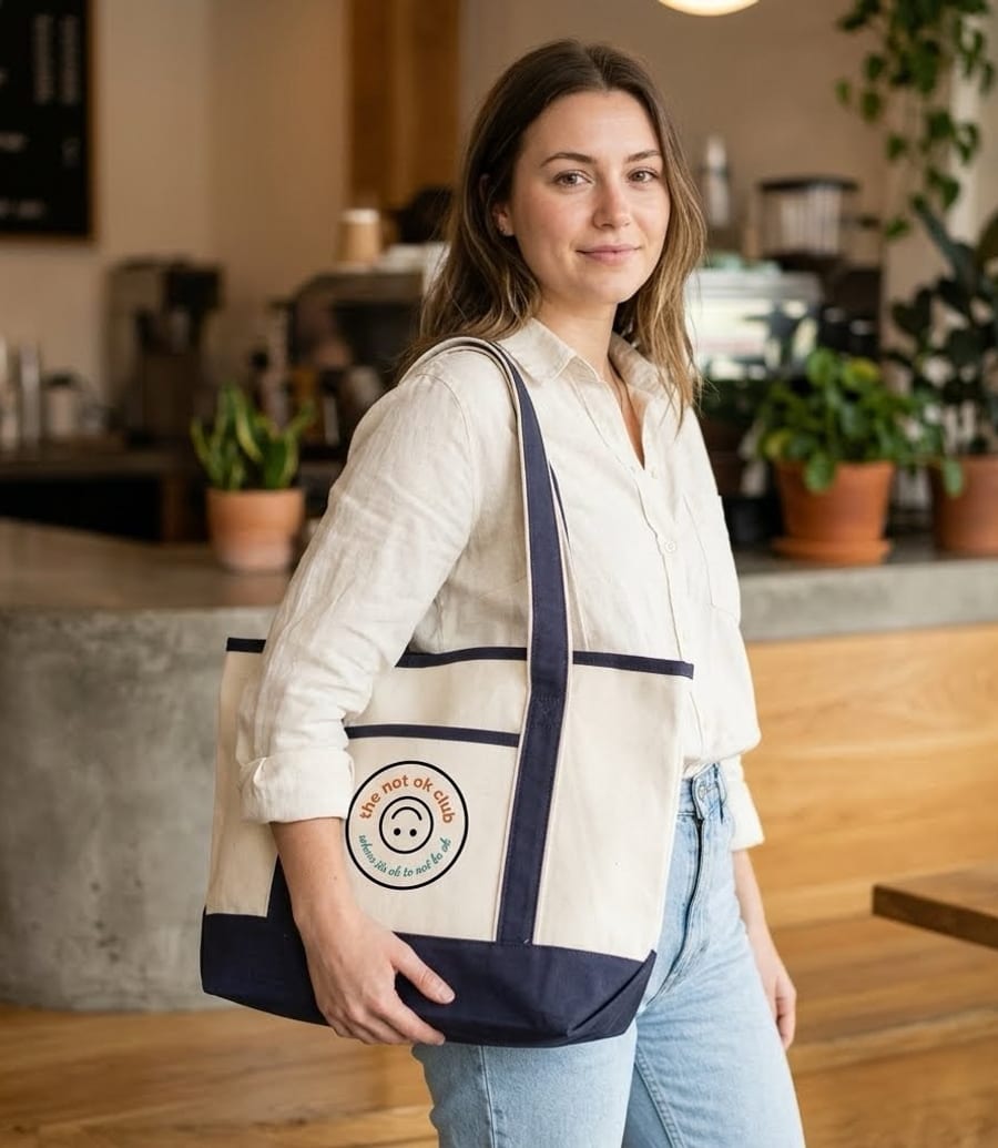 a woman carrying the not ok club cream-and-navy canvas tote with the seal logo